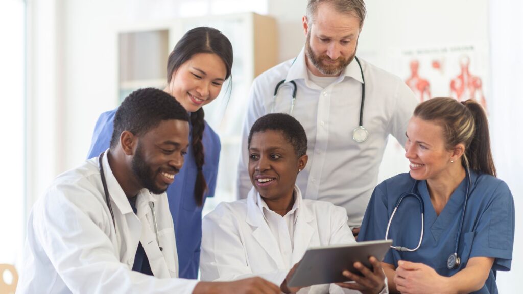 Médicos sentados em um consultório, sorrindo e conversando sobre algo apresentado em um tablet.