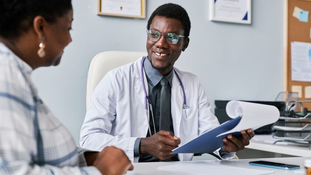 Médico negro em um consultório conversando com outra profissional negra.