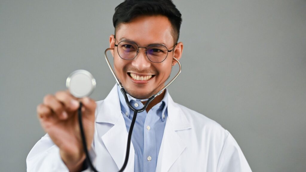 Médico novo sorrindo e levantando um estetoscópio preto.
